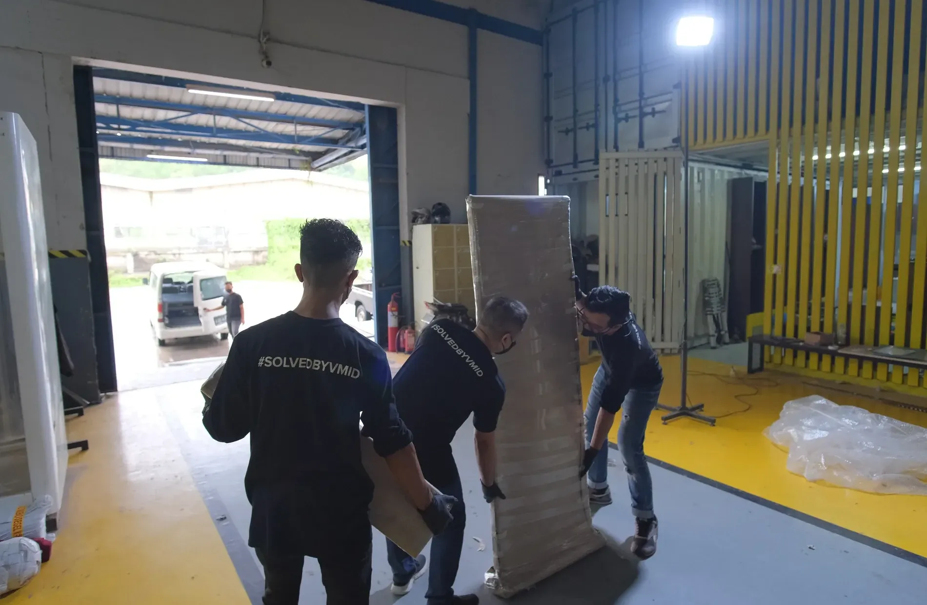 Crew carrying a tall wrapped panel toward the open loading bay, a van parked outside