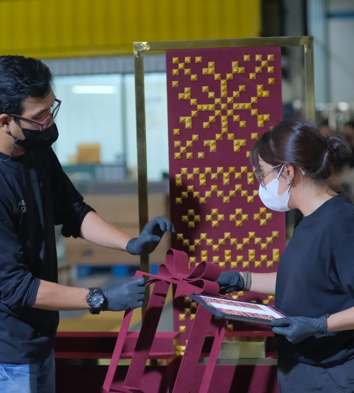Two VMID crew members fitting gold studs onto a maroon snowflake panel while checking a tablet with the design spec