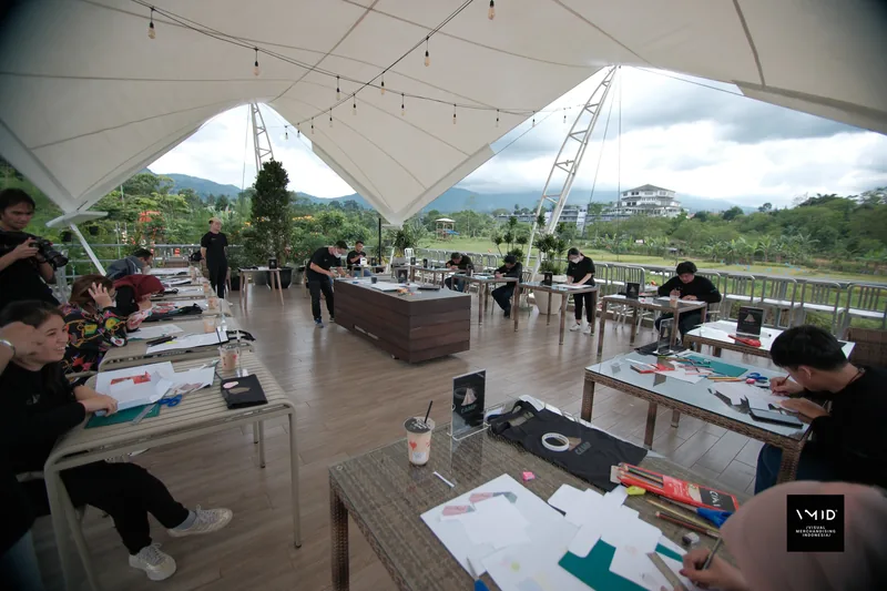 Participants drawing and cutting paper at their own worktables under an open-air canopy — CAMP, PT. Agrinesia Raya 2023