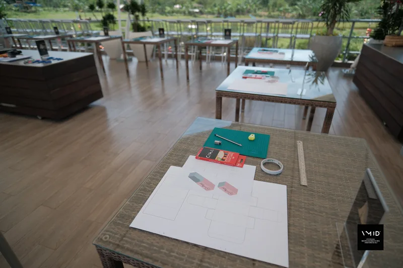 A worktable laid out with a cutting mat, pencils, tape, a steel ruler and a paper box template — CAMP 2023
