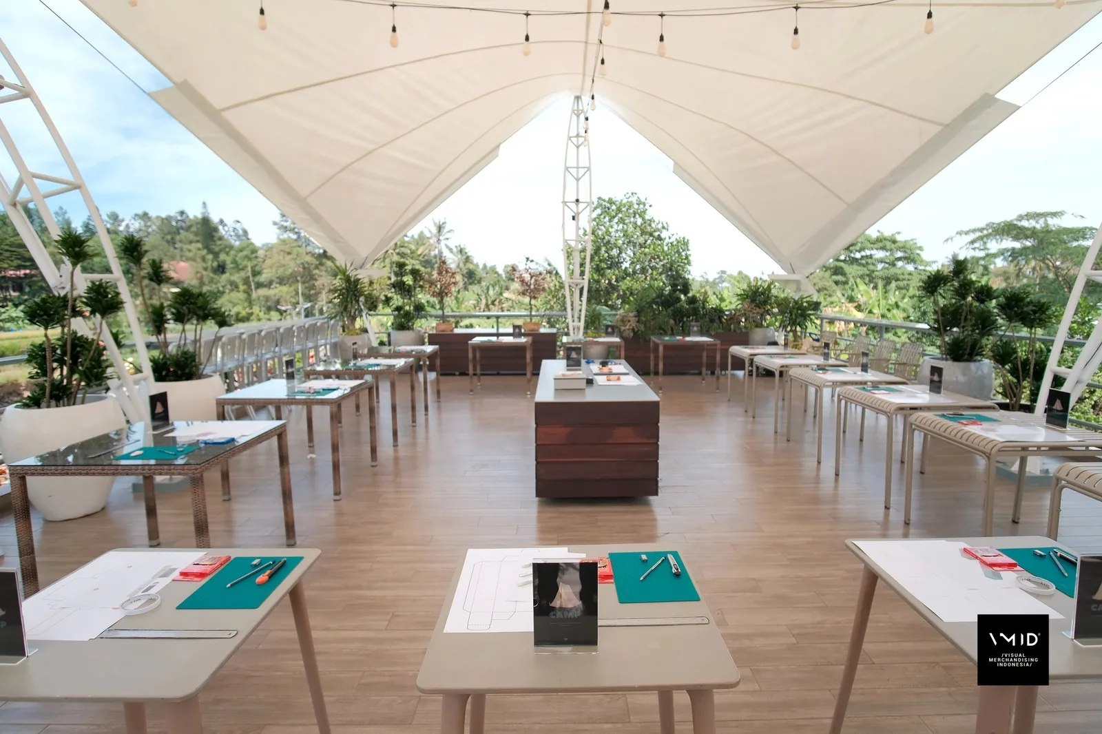 Worktables set with cutting mats, rulers and paper under a white canopy, ready for CAMP — PT. Agrinesia Raya, 2023