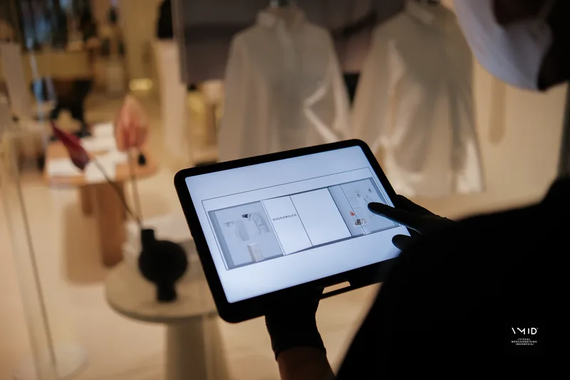 A gloved hand holding a tablet open on a product layout, the white shirts of the window out of focus behind — Masshiro&Co., 2022