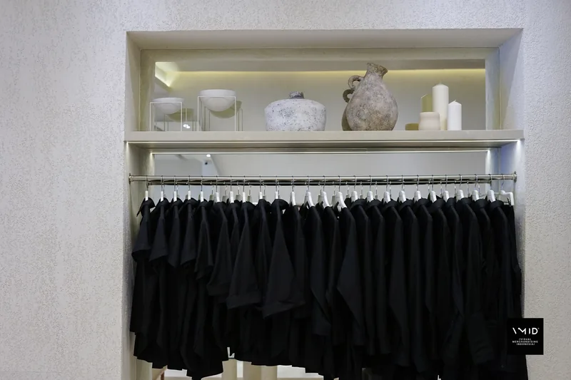 Black shirts on a rail below a lit shelf of stone vases, bowls and candles — Masshiro&Co., 2022