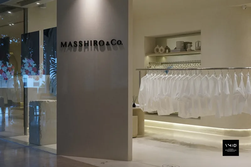 The Masshiro&Co. name on a grey pillar at the entrance, a long rail of white shirts behind under a shelf of ceramics — 2022