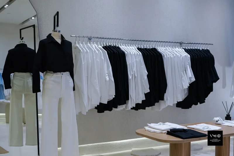 Two mannequins in black shirts and white trousers beside a rail alternating white and black shirts — Masshiro&Co., 2022