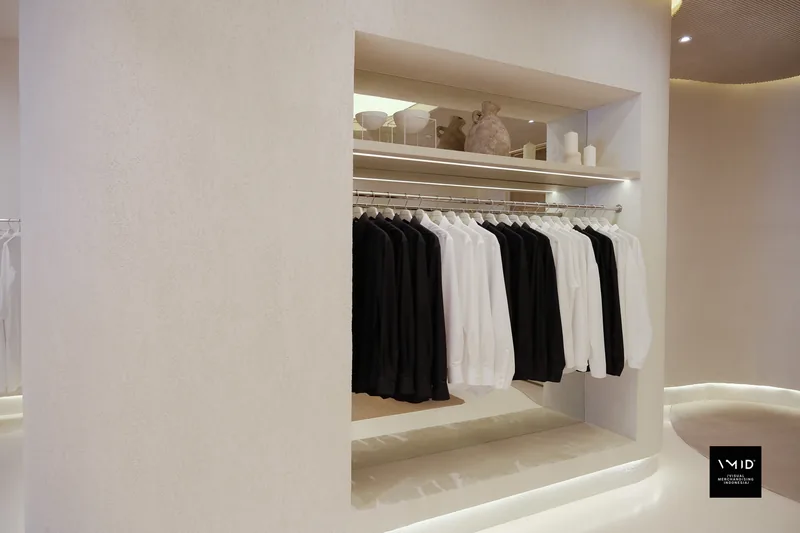 A lit wall niche of black and white shirts under a shelf of pale ceramics — Masshiro&Co., 2022