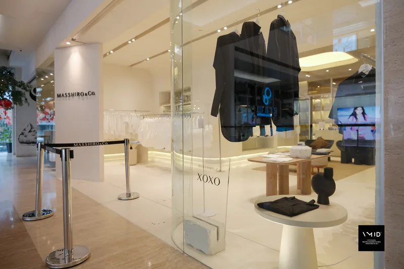 The Masshiro&Co. storefront: XOXO lettering on the glass, a black shirt suspended in the window and a round plinth of folded pieces — 2022