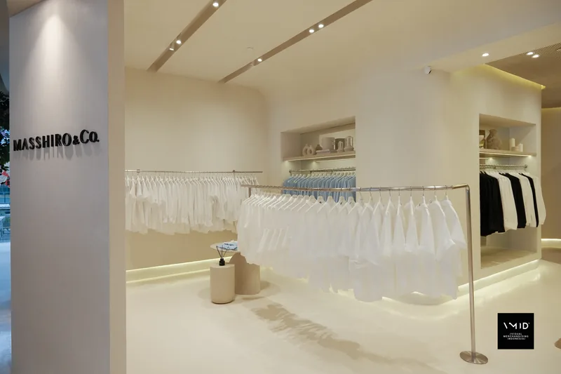White shirts on curved rails and a rail of blue shirts beyond, black and white pieces in the far niche — inside Masshiro&Co., 2022